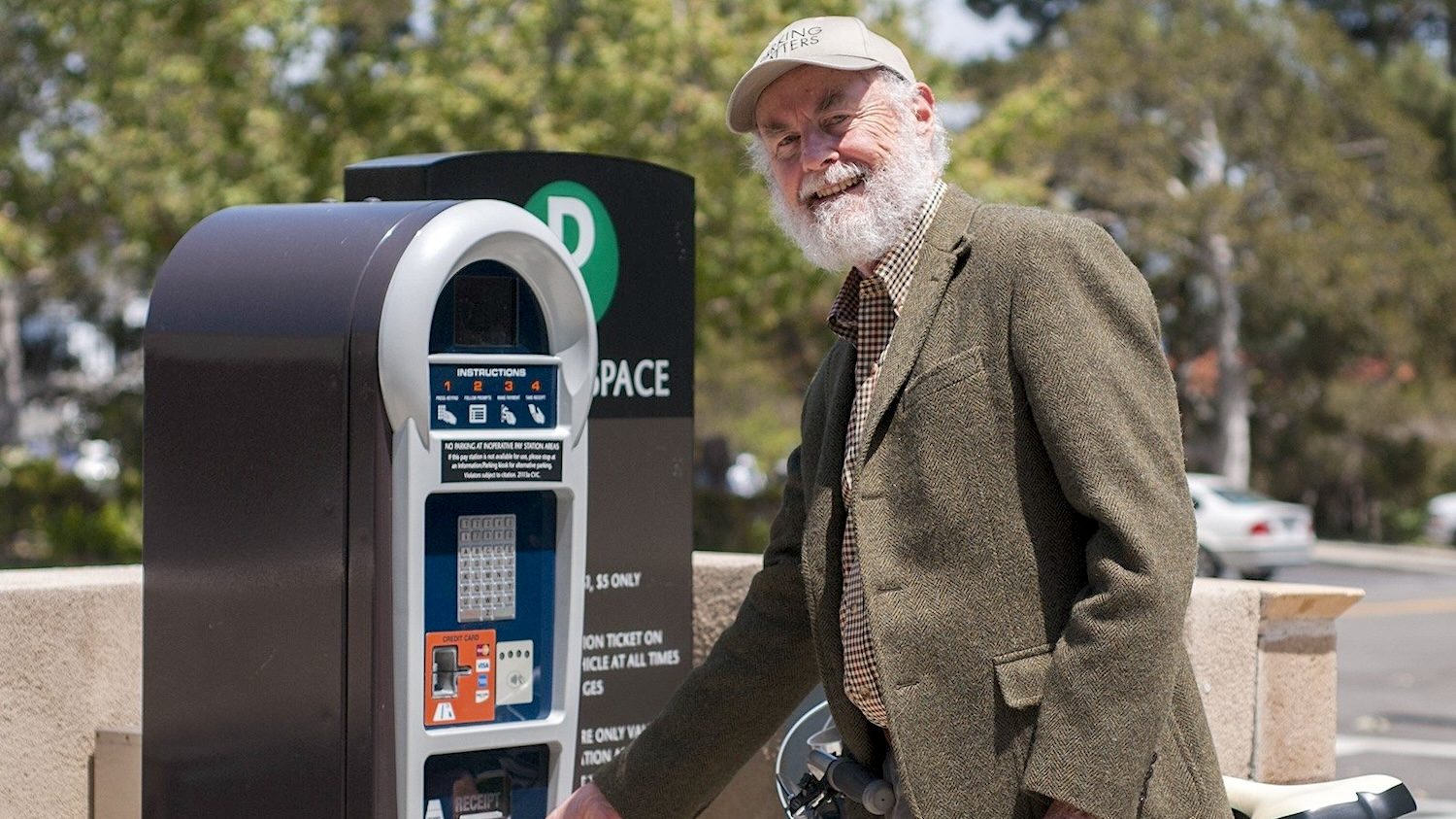 Donald Shoup poses smiling while inserting cash into a parking payment machine